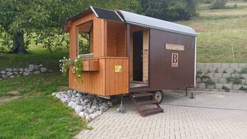 Ein Wohnmobil aus Holz mit überdachter Veranda und einem Schild, das es als 'Bauwagenhaus' kennzeichnet.