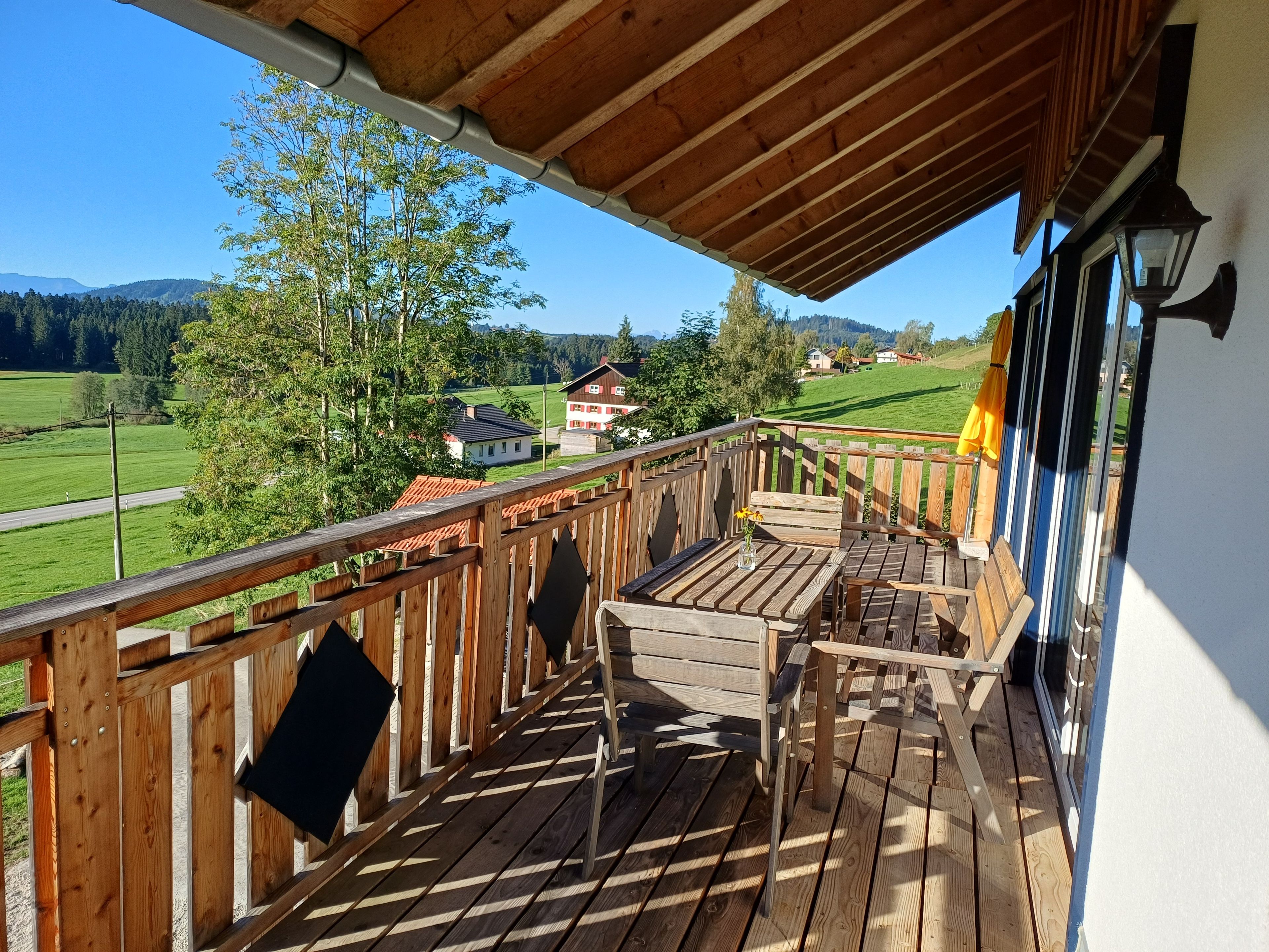 Eine Holzterrasse mit Tisch und Stühlen, die auf eine grüne Landschaft mit Häusern blickt.