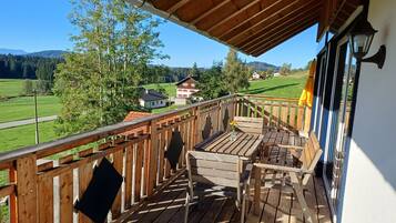 Eine Holzterrasse mit Tisch und Stühlen, die auf eine grüne Landschaft mit Häusern blickt.