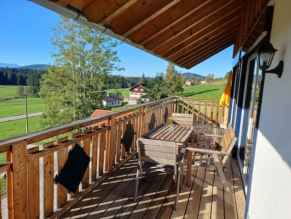 A wooden deck with a table and chairs, overlooking a green landscape with houses.