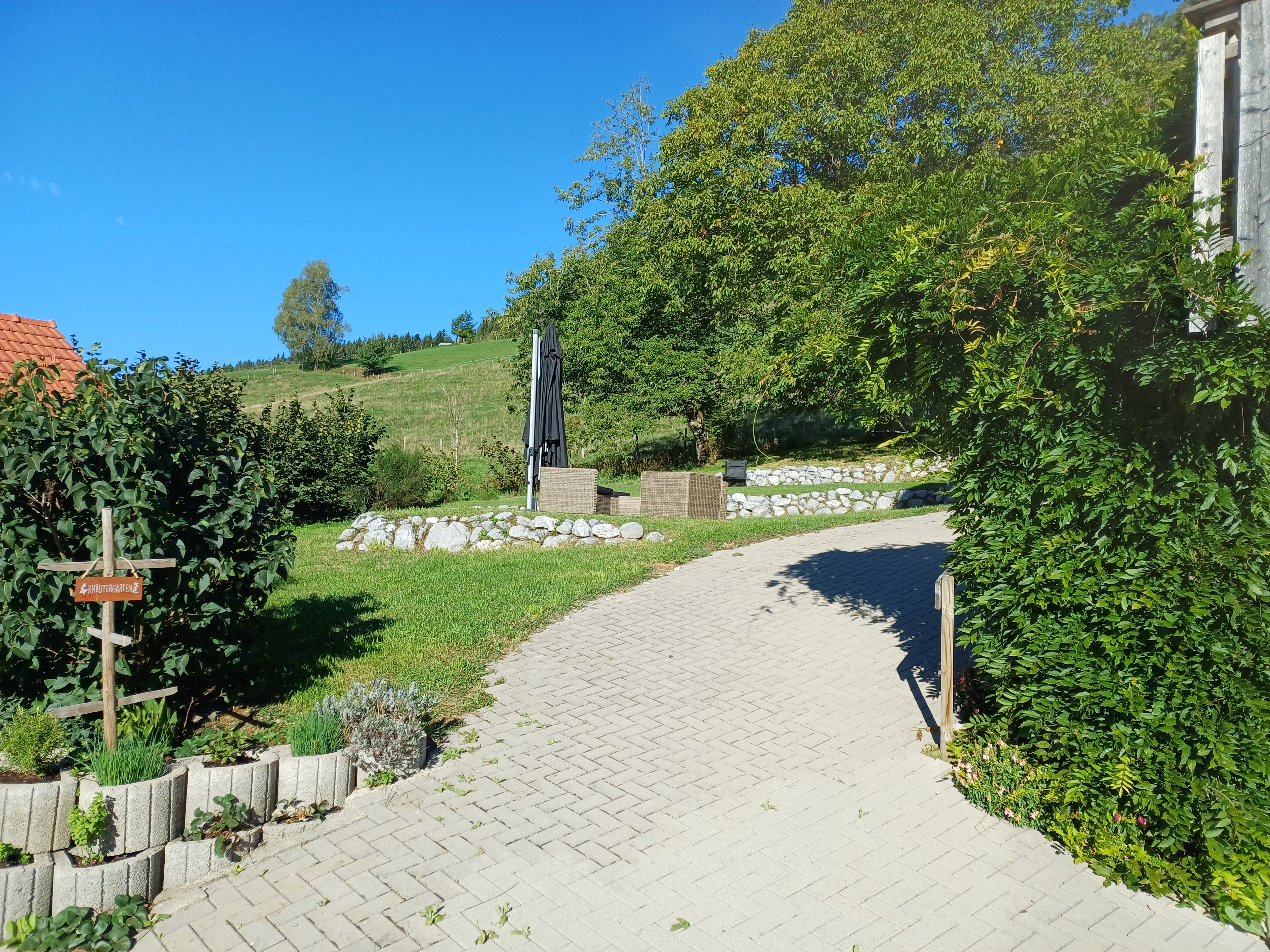 Ein gepflasterter Weg führt durch eine angelegte Grünfläche mit einer Steinmauer und Pflanzen.