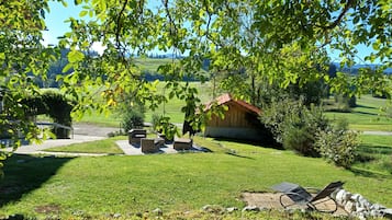 Eine grüne Außengelände mit einer Holzkonstruktion, Sitzgelegenheiten im Freien und Blick auf eine hügelige Landschaft.