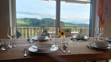 A dining table set for four with a view of a wooden deck and a forested landscape.