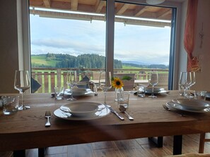A dining table set for four with a view of a wooden deck and a forested landscape.