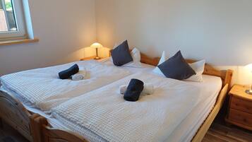 A double bed with a white textured bedspread, two pillows, a folded towel, and a bedside table with a lamp.