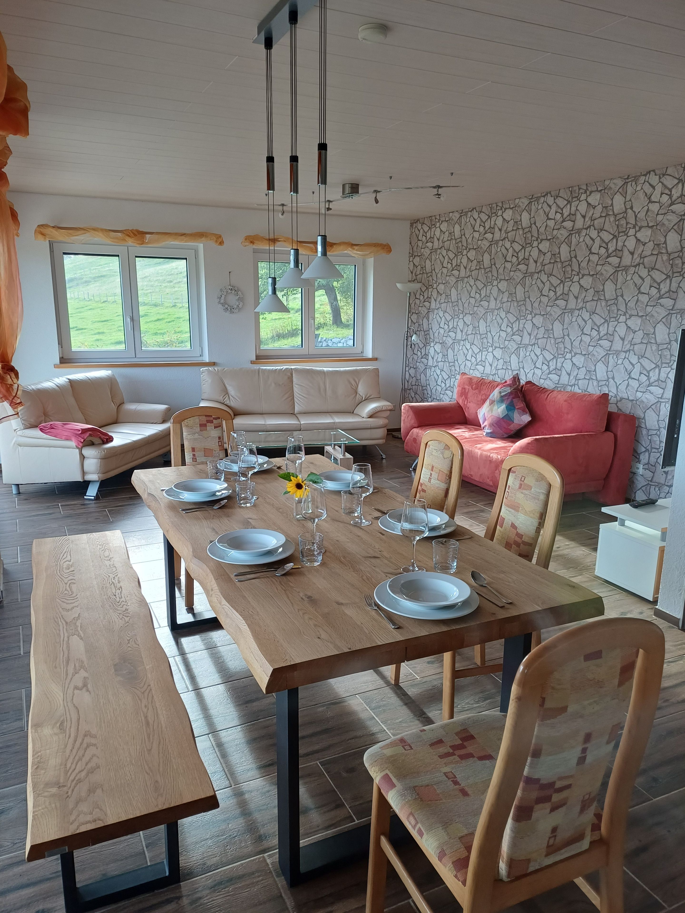 A dining area with a wooden table set for four, a bench, and a sofa in the background.
