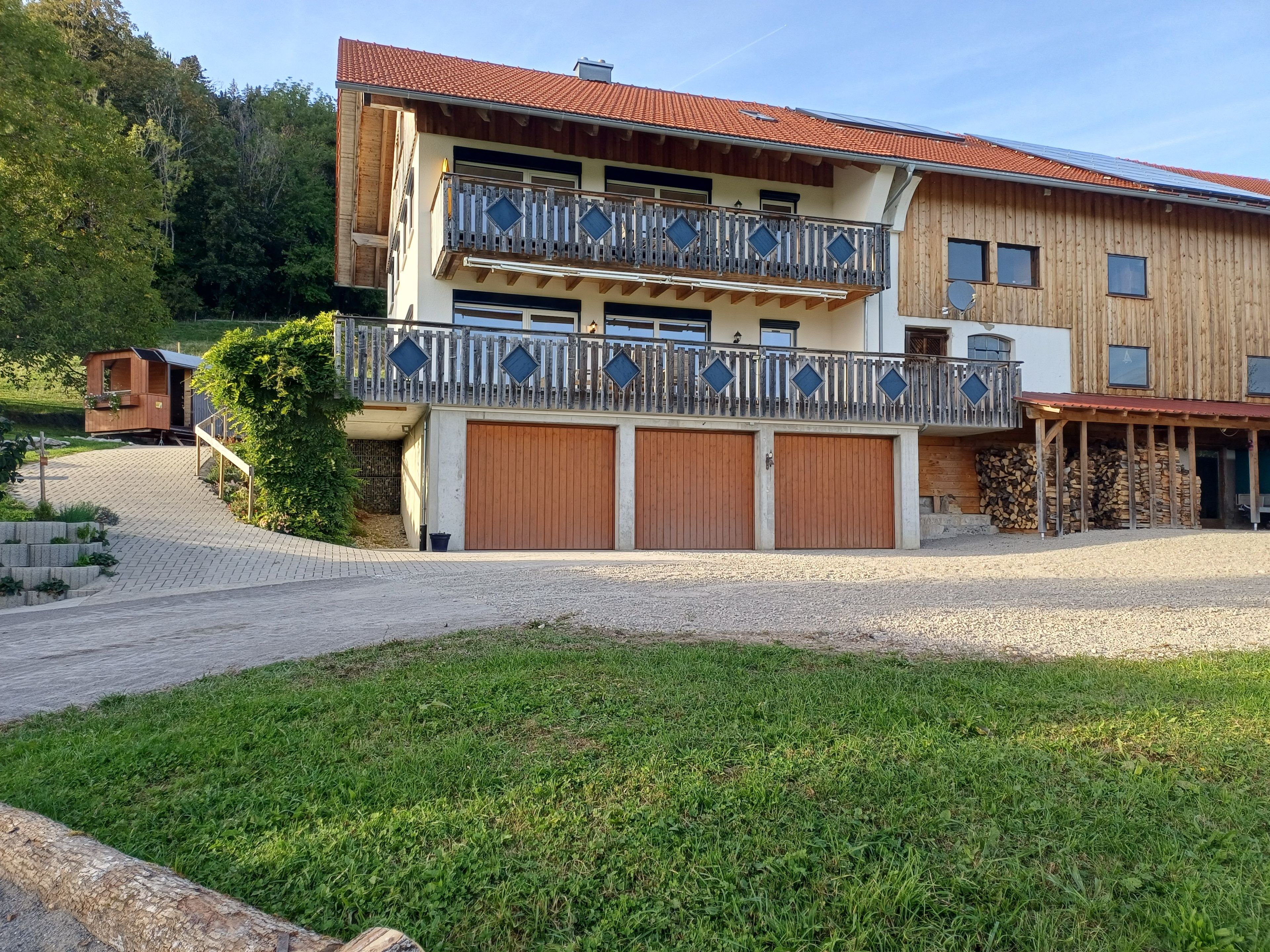 Ein zweistöckiges Gebäude mit Balkon, überdachter Auffahrt und Holzstapel.