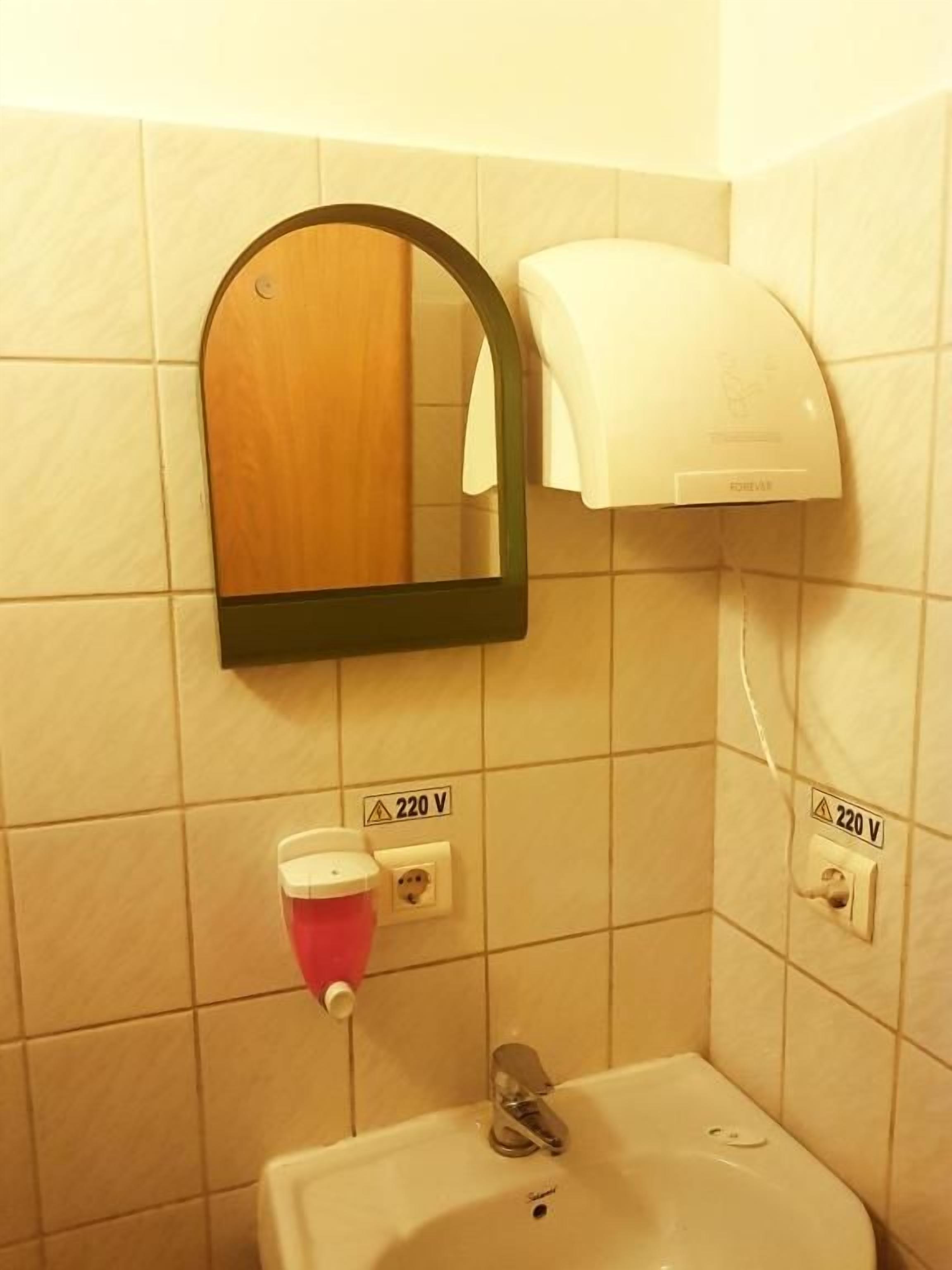 Un baño con lavamanos, espejo, dispensador de toallas y toma de corriente.