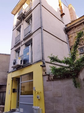 Un edificio con fachada amarilla, entrada a nivel de calle y una ventana con un letrero.