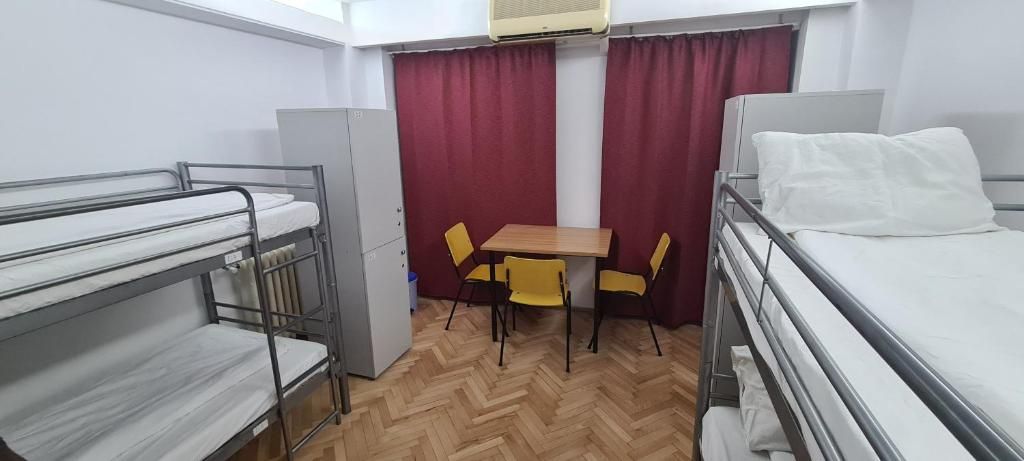 Un dormitorio con literas, una mesa con sillas y un ventanal con cortinas.