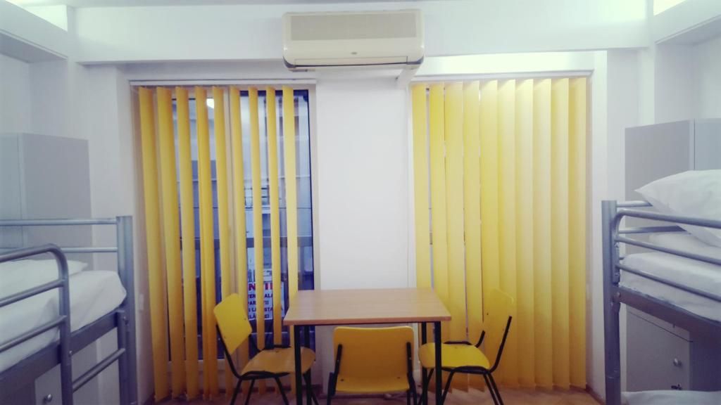 Una habitación con literas, una mesa, dos sillas y cortinas amarillas.