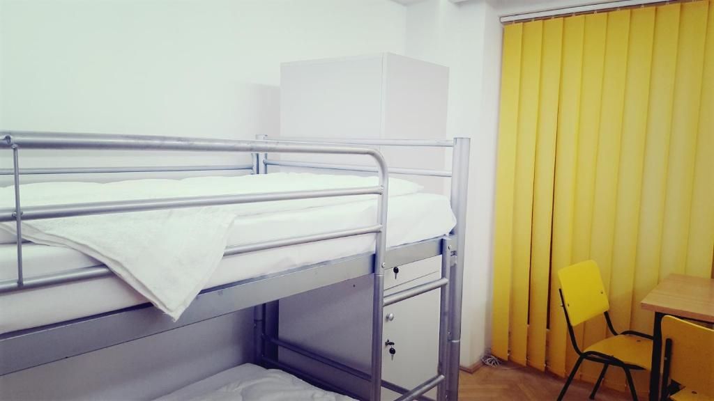 Uma cama beliche com uma cama inferior, uma mesinha, uma cadeira e uma cortina amarela.
