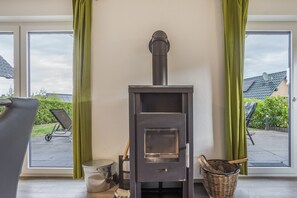 Una habitación con estufa de leña, ventana con cortinas y vistas al exterior.