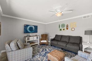 A living room with a grey sofa, patterned armchairs, a television, a ceiling fan, and decorative wall art. - Seascape Villa 95E *Newly updated and quiet villa with beach access* (Miramar Beach)