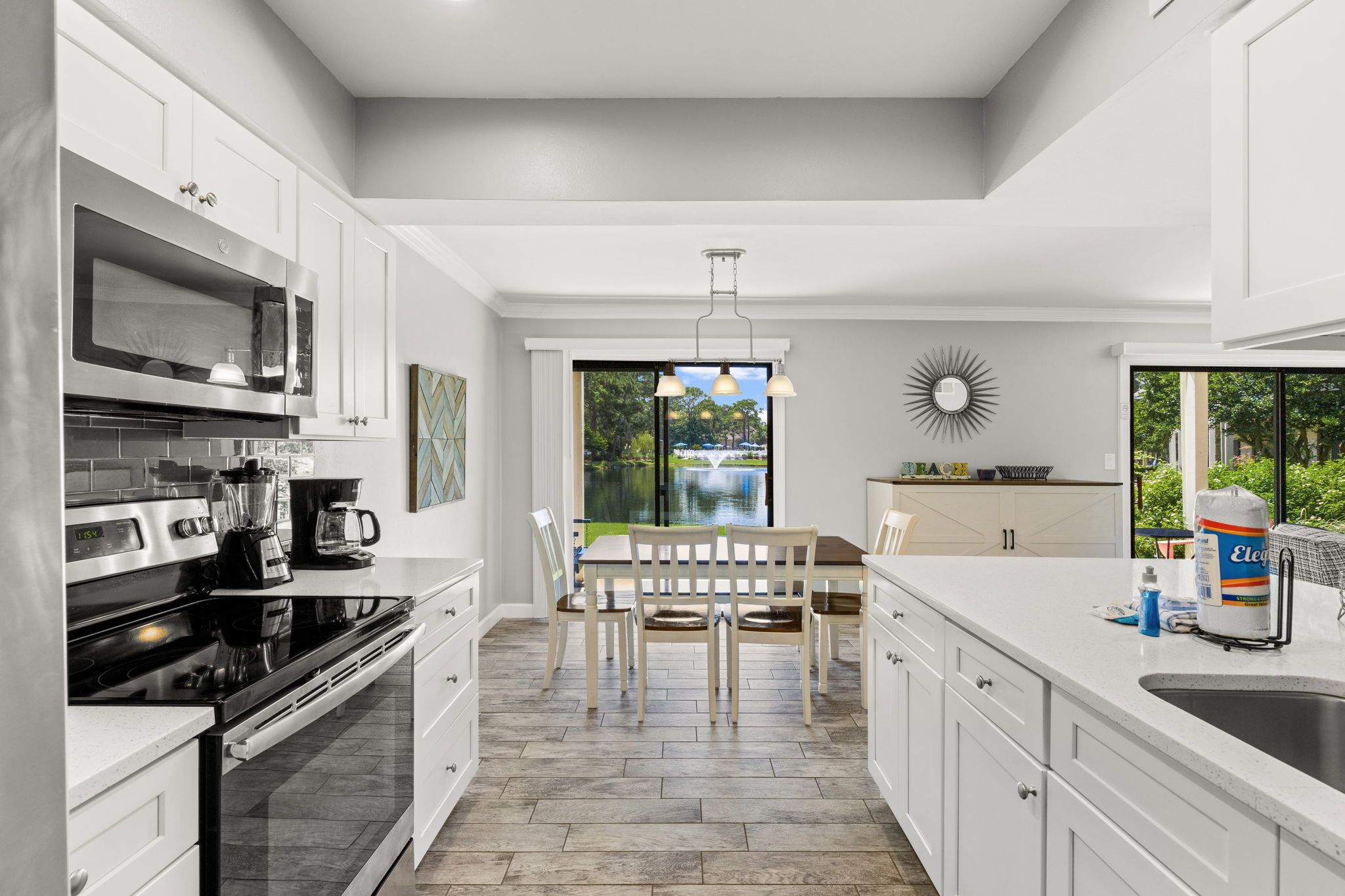 A modern kitchen with white cabinetry, a dining area with a table and chairs, and a view of a garden through large windows.