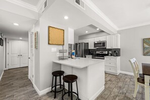 A modern kitchen with white cabinetry, a central island with stools, a stainless steel refrigerator, and a microwave. - Seascape Villa 95E *Newly updated and quiet villa with beach access* (Miramar Beach)