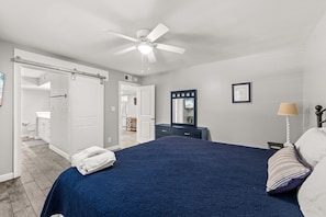 A bedroom with a bed, a dresser, a mirror, a ceiling fan, and a door leading to another room. - Seascape Villa 95E *Newly updated and quiet villa with beach access* (Miramar Beach)