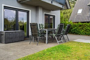 Un patio exterior con una mesa y sillas, un calentador incorporado y vistas a una casa con tejado de tejas.