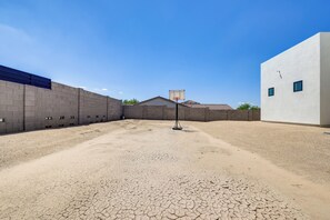 An outdoor basketball court with a hoop, surrounded by a gravel surface and adjacent buildings. - 1 Mi to South Mtn Park! Home w/ Poolside Oasis (Phoenix)