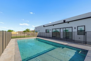 A swimming pool with a clear blue water surface, surrounded by a paved deck and a modern building with large windows and a flat roof. - 1 Mi to South Mtn Park! Home w/ Poolside Oasis (Phoenix)