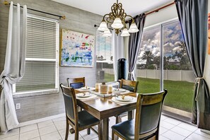 Ein Essbereich mit einem Holztisch, gedeckt für zwei Personen, einem Bild an der Wand und Blick ins Freie durch große Fenster.