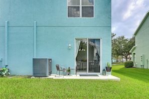 Een gebouw met een blauwe gevel, een glazen schuifdeur, een klein terras met een tafel en stoelen, en een grote airconditioning.