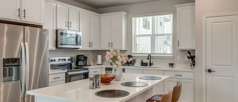 A modern kitchen with white cabinetry, stainless steel appliances, a central island with stools, and a window providing natural light.