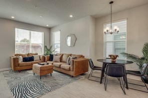 A modern living room with a sectional sofa, a coffee table, and a dining area with a glass table and chairs. - City Skyline Views! Modern Dtwn Jax Townhome (Jacksonville)