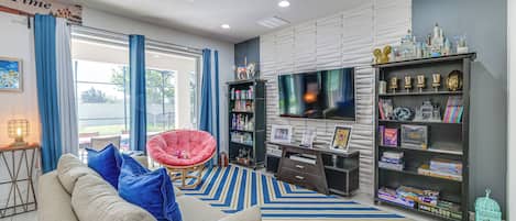 A living room with a sofa, a red chair, a TV, a bookshelf, and a window with curtains.