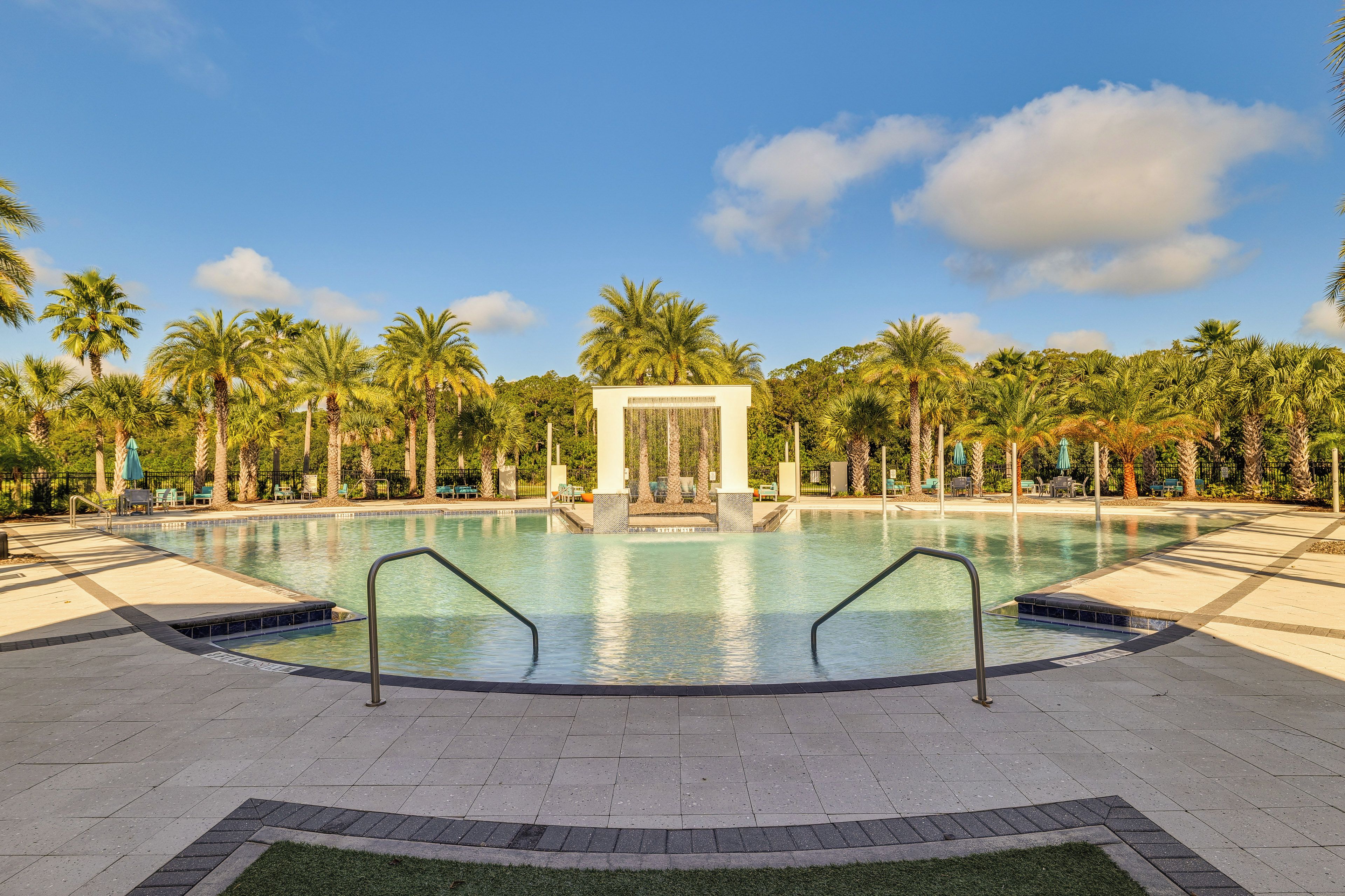 A swimming pool with a clear view of the sky, surrounded by palm trees and a white structure in the center.