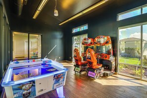 A room with a foosball table, arcade games, and a view of the outdoors. - 8 Mi to Disney! Whimsical Home w/ Pool & Game Room (Kissimmee)