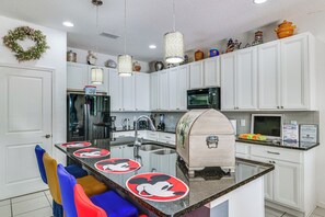 A kitchen with white cabinets, a stainless steel refrigerator, a microwave, and a coffee maker. - 8 Mi to Disney! Whimsical Home w/ Pool & Game Room (Kissimmee)