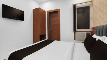 Una habitación de hotel con una cama, un televisor de pantalla plana montado en la pared, una ventana con persianas y un equipo de aire acondicionado incorporado.