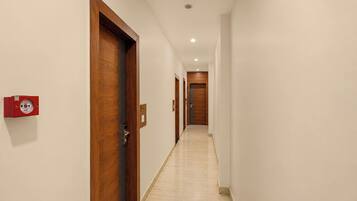 Un pasillo con puertas de madera, un detector de incendios y un piso limpio con baldosas.