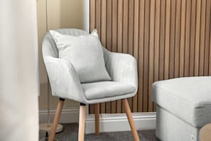 A modern armchair with wooden legs and a grey cushion, positioned in a room with a wooden slat wall and a grey carpet. - Stylish Brick Lane Apartment Sleeps 9 Shoreditch (Greater London)