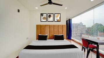 A hotel room with a bed, ceiling fan, artwork, and a view of the city.