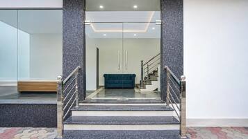 Un interior moderno con una escalera que conduce a una sala de estar, con un sofá azul verdoso y un separador de vidrio.