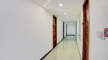 Un pasillo con paredes blancas, puertas de madera y piso de mármol.