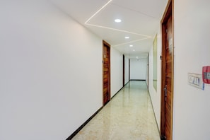 Un pasillo con paredes blancas, puertas de madera y piso de mármol.