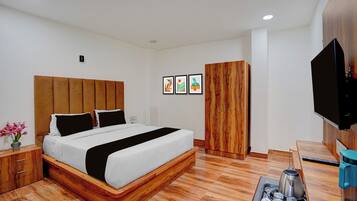 A modern hotel room with a wooden bed frame, a flat-screen TV, a wooden wardrobe, and a coffee table with a kettle and cups.