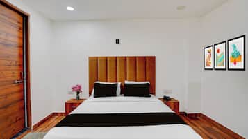 Quarto de hotel com cabeceira de madeira, cama com roupa de cama preta e branca, mesa de cabeceira com telefone e parede com três obras de arte emolduradas.