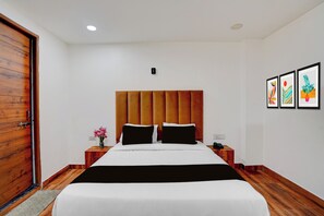 Habitación de hotel con cabecera de madera, cama con ropa de cama blanca y negra, mesita de noche con un teléfono y una pared con tres obras de arte enmarcadas.