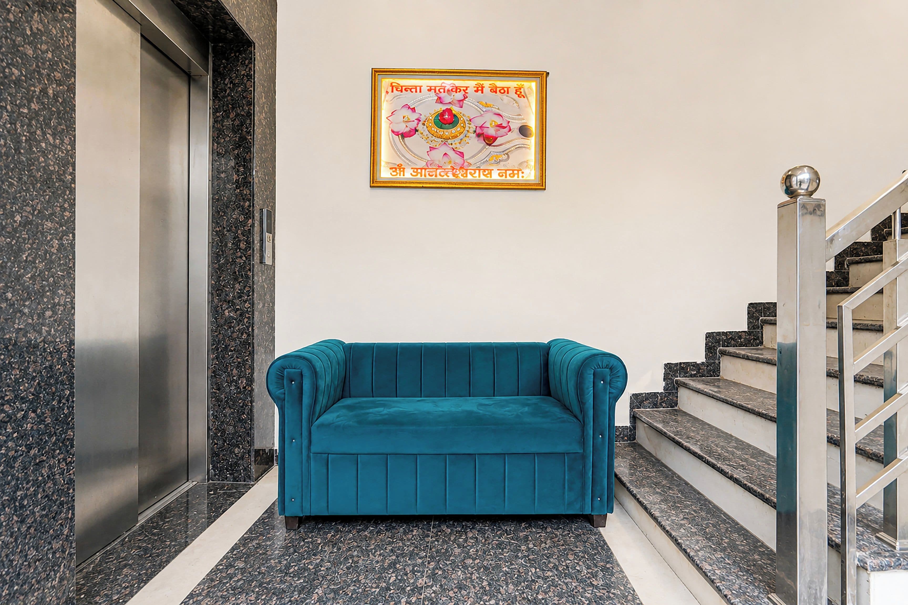 Un ascensor, un sofá color turquesa y una escalera con barandilla de metal.