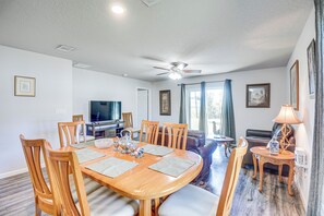Uma sala de jantar com uma mesa de madeira, cadeiras e uma televisão ao fundo.