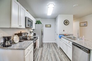 A kitchen with white cabinets, stainless steel appliances, a granite countertop, and a wooden floor. - 7 Mi to Beach! Group & Pet-friendly Palm Coast Gem (Palm Coast)