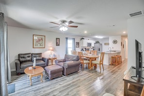 A living room with a ceiling fan, a dining area with wooden chairs, and a kitchen in the background. - 7 Mi to Beach! Group & Pet-friendly Palm Coast Gem (Palm Coast)