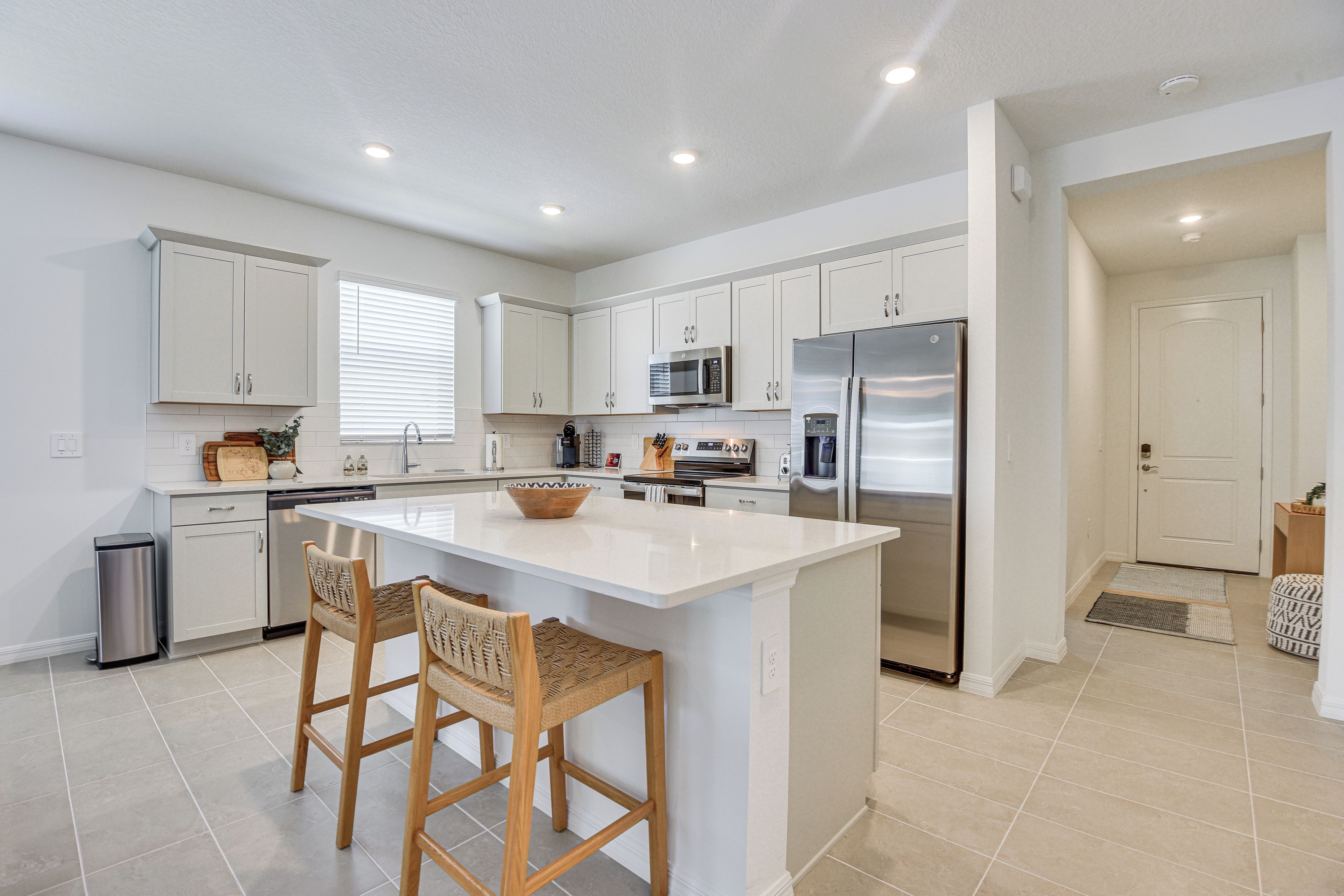 A modern kitchen with white cabinetry, a central island with bar stools, stainless steel appliances, and recessed ceiling lighting.