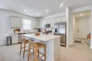 A modern kitchen with white cabinetry, a central island with bar stools, stainless steel appliances, and recessed ceiling lighting. - Private Community w/ Pool, Near Gulf Beaches (Palmetto)