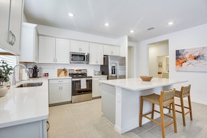 A modern kitchen with white cabinetry, stainless steel appliances, and a central island with bar stools. - Private Community w/ Pool, Near Gulf Beaches (Palmetto)