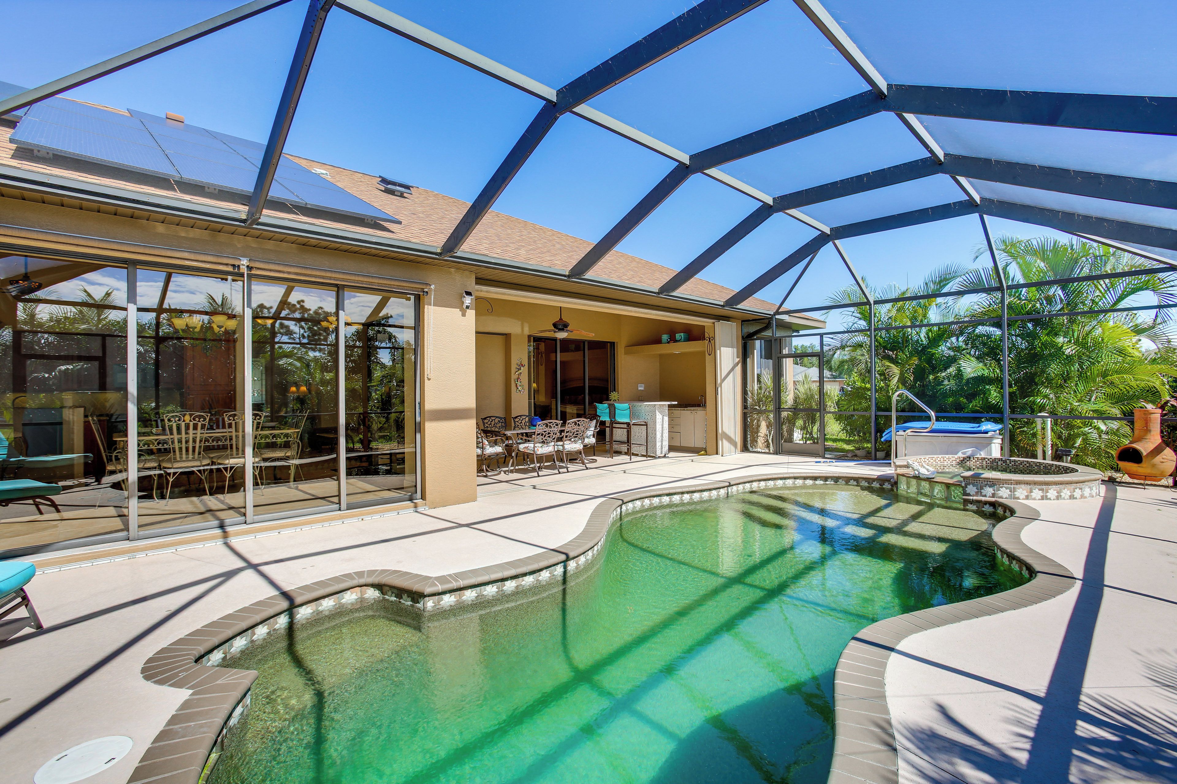 A pool area with a glass enclosure, a patio with outdoor furniture, and a view of the surrounding landscape.